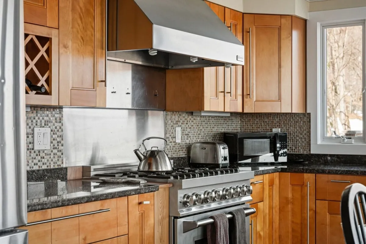 A spacious kitchen with a sleek stainless steel range, granite countertops, warm wood cabinetry, and a kettle on the stove, set up for entertaining and intimate meals. The atmosphere is inviting and perfect for pre- or post-dining socializing.