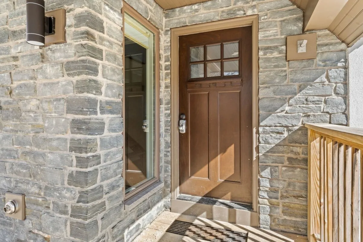The front approach to the home features a sturdy wooden door, stone accents, and warm natural lighting streaming through windows, offering a sense of privacy and exclusive retreat.
