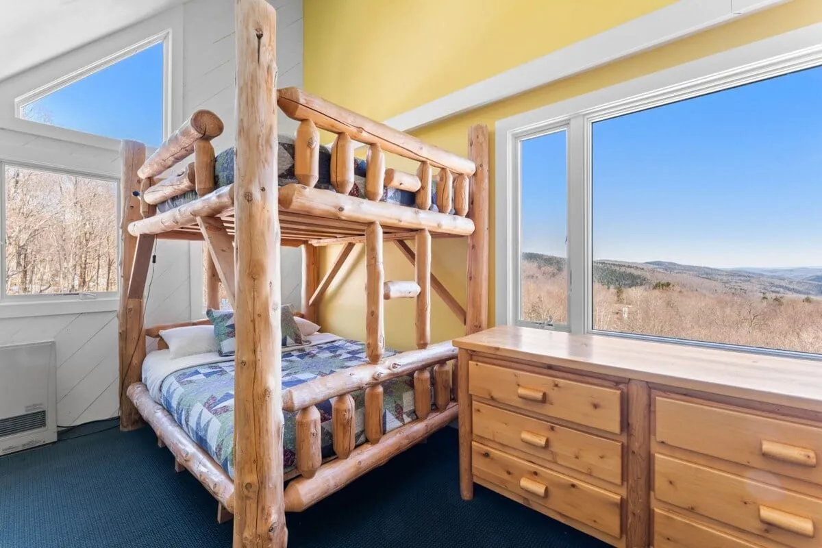 A playful yet serene nook featuring a stylish wooden bunk bed and a large window that floods the room with soft, natural morning light. The wooden dresser adds a touch of practicality and charm. The space feels inviting for kids and the young-at-heart, echoing a sense of adventure and cozy storytelling moments.
