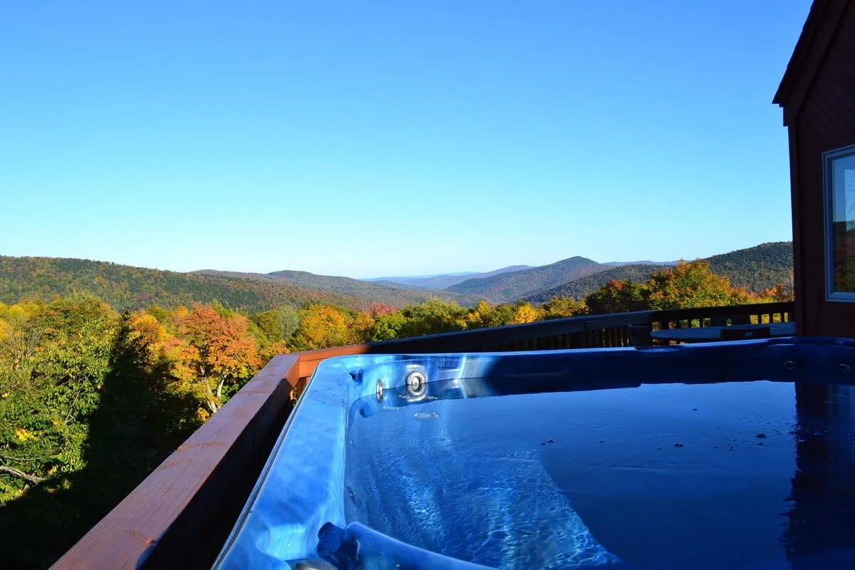 This image features a private hot tub set on a deck, overlooking a sweeping view of Vermont's autumn foliage and distant mountains. The warm glow of the hot tub contrasts beautifully with the vibrant colors of the leaves, inviting relaxation and a sense of outdoor luxury.