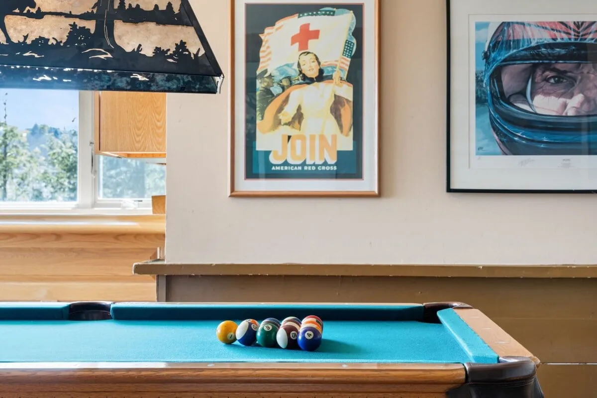 This image showcases a lively game room centered around a pool table, complemented by vintage posters and a distinctive hanging light fixture. The scene captures guests engaged in playing pool, chatting, and unwinding, evoking a playful and nostalgic atmosphere.
